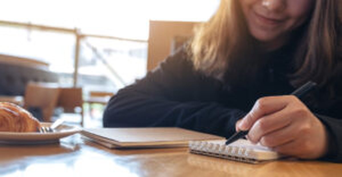 Autora escrevendo à mão num caderno, num café